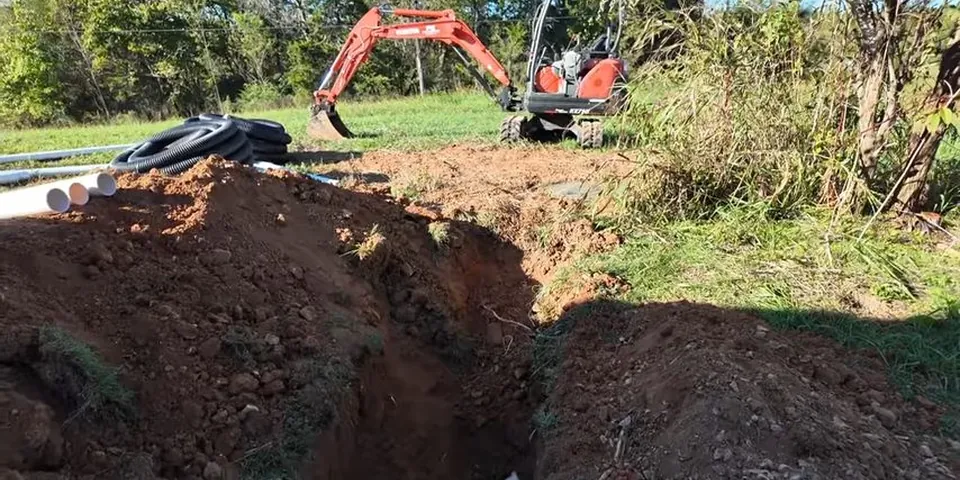 Excavator opening a yard trench for buried pipe work for Plumbing Service in the South Street Corridor, Lakewood CA